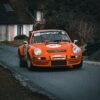 A vintage orange racing car maneuvers through a rural road, showcasing speed and retro design.
