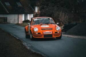 A vintage orange racing car maneuvers through a rural road, showcasing speed and retro design.