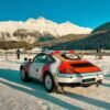 Racing car parked in a snowy mountain landscape with people enjoying winter activities.