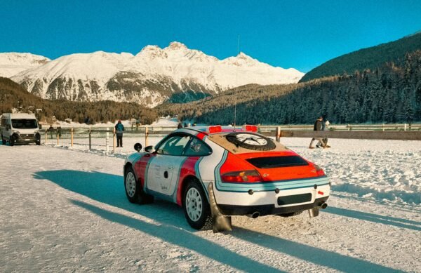 Racing car parked in a snowy mountain landscape with people enjoying winter activities.